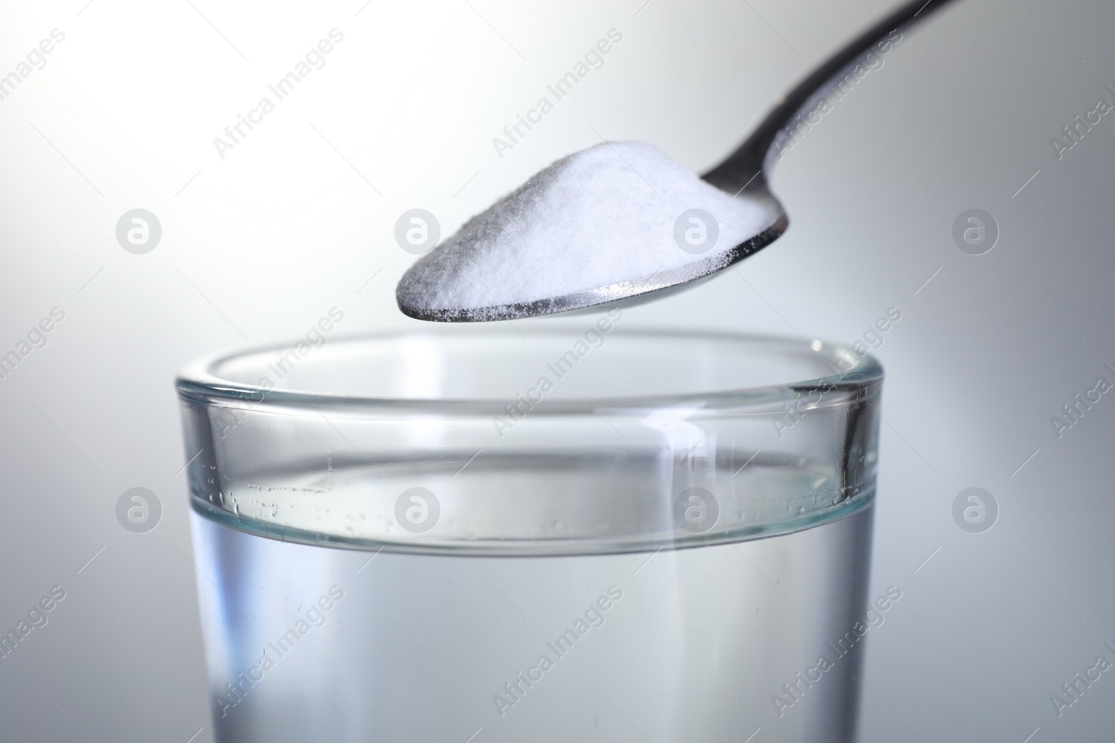 Photo of Spoon with baking soda over glass of water on light grey background, closeup