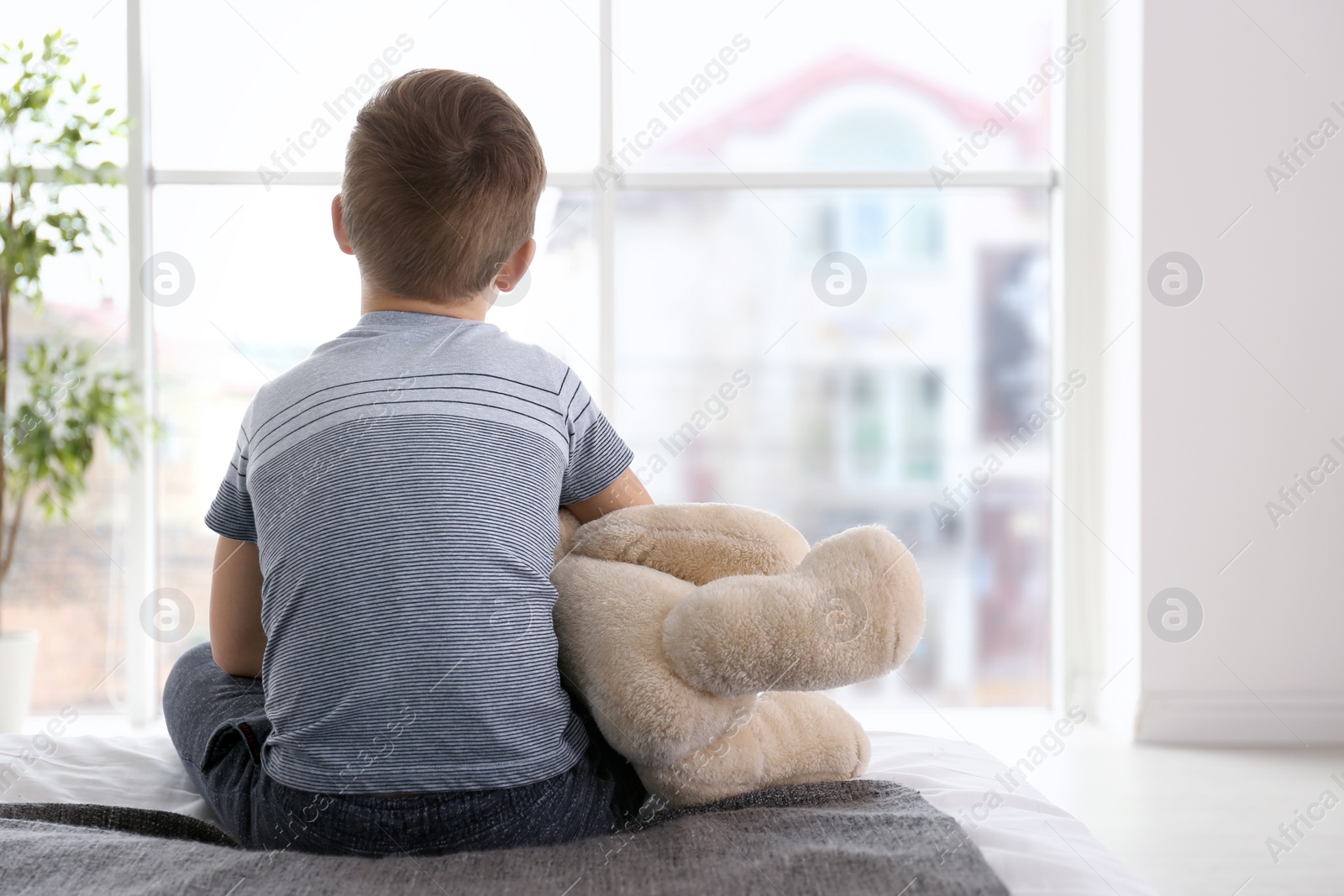 Photo of Lonely little boy sitting on bed in room. Autism concept