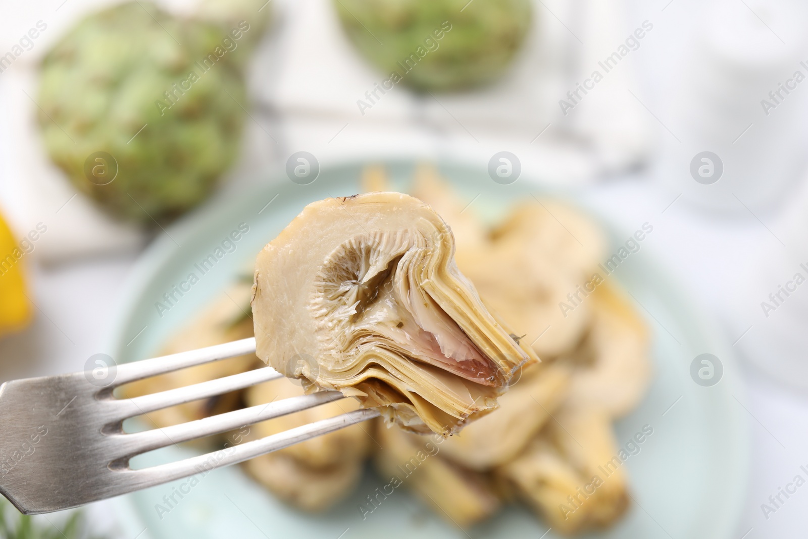 Photo of Fork with delicious pickled artichoke over table, closeup