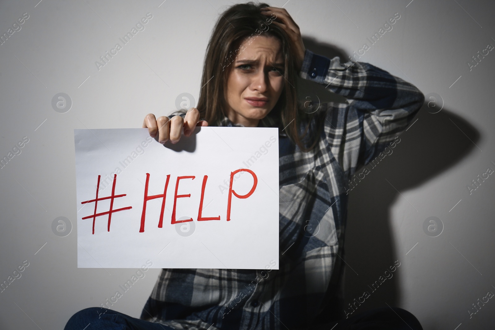 Photo of Crying young woman with hashtag HELP near white wall. Domestic violence concept