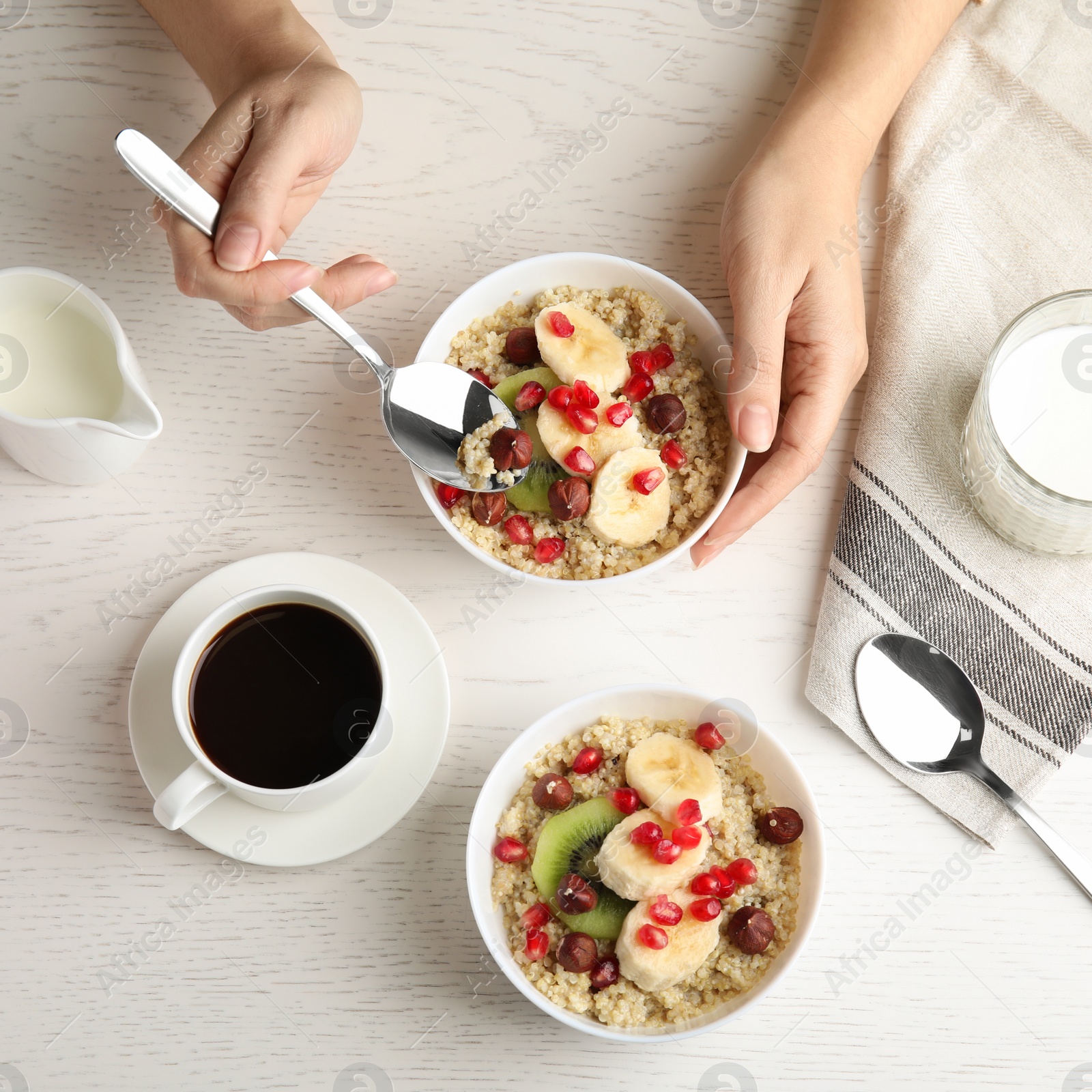 Photo of Woman eating quinoa porridge with hazelnuts, kiwi, banana and pomegranate seeds at wooden table, top view