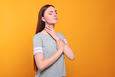 Photo of Young woman with sore throat on orange background. Space for text