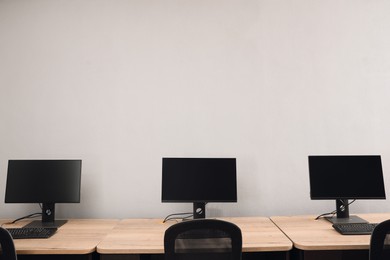 Photo of Open office interior. Modern workplaces with computers near light grey wall