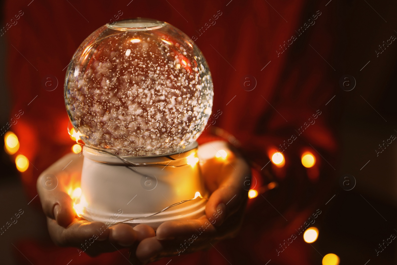 Photo of Woman holding snow globe and Christmas lights in darkness, closeup
