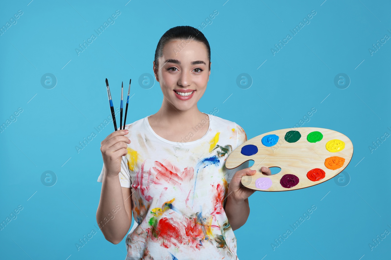 Photo of Woman with painting tools on light blue background. Young artist