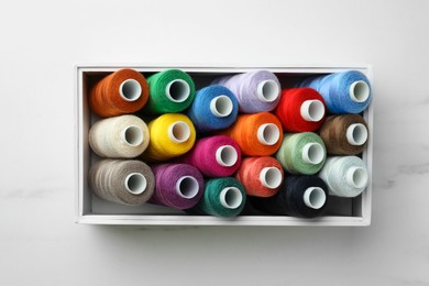 Photo of Box with colorful sewing threads on white marble table, top view