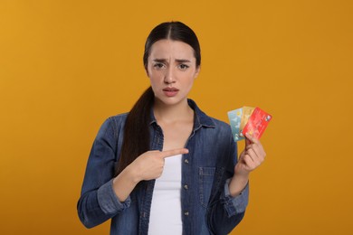 Confused woman pointing at credit cards on orange background. Debt problem