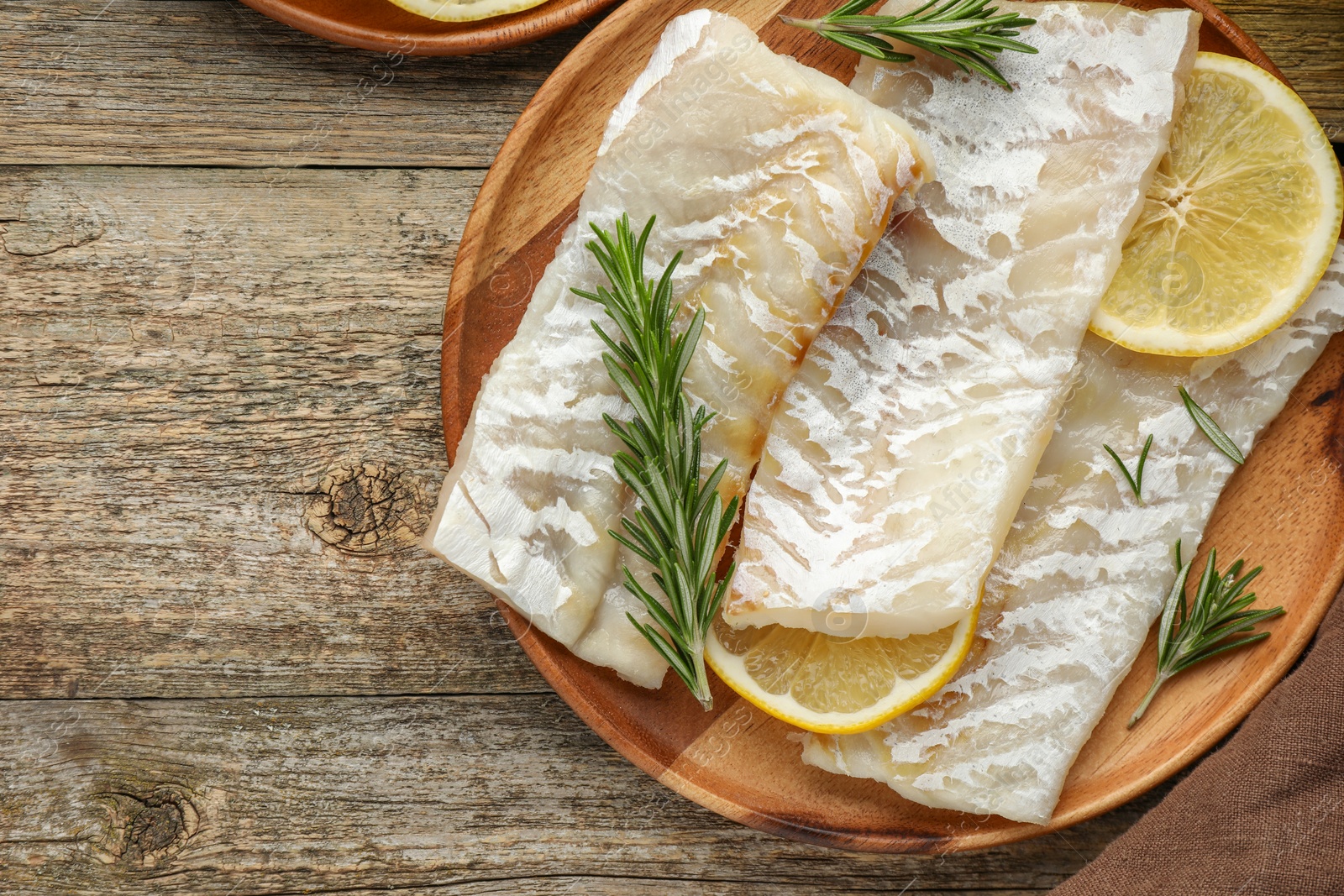 Photo of Fresh raw cod fillets with rosemary and lemon on wooden table, flat lay. Space for text