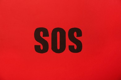 Photo of Abbreviation SOS (Save Our Souls) written on red background, top view