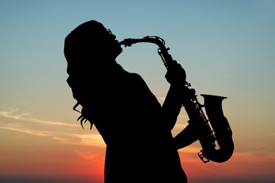 Image of Silhouette of woman playing saxophone against beautiful sky at sunset