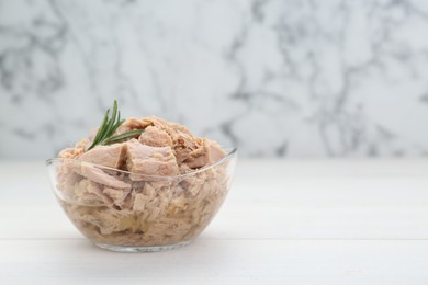 Bowl with canned tuna and rosemary on wooden table near white marble wall, space for text