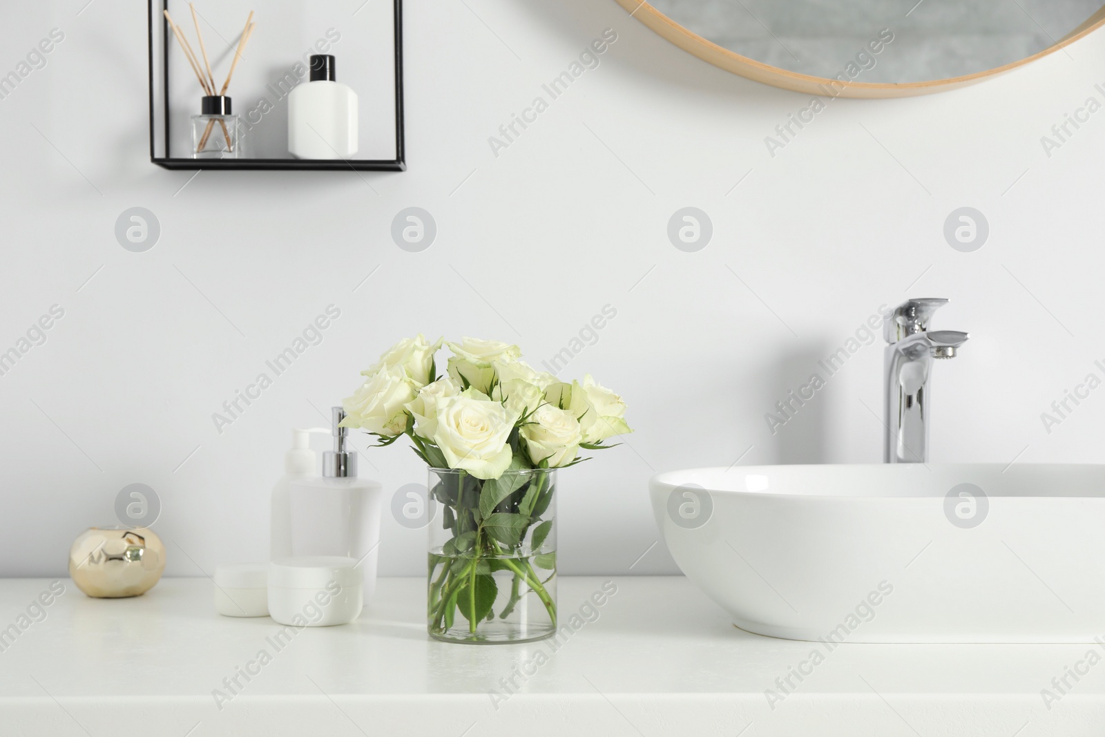 Photo of Bouquet of beautiful roses in vase and bath accessories near sink in bathroom