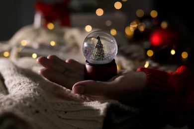 Woman holding Christmas snow globe on blurred background, closeup