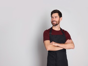 Professional hairdresser wearing apron with on light grey background, space for text