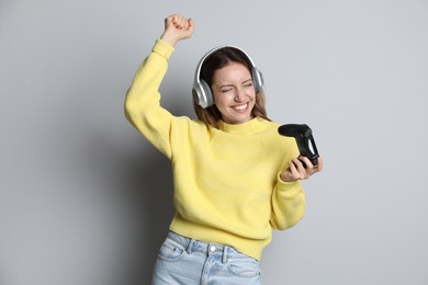 Happy woman in headphones with game controller on light grey background