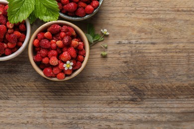 Fresh wild strawberries in bowls and leaves on wooden table, flat lay. Space for text