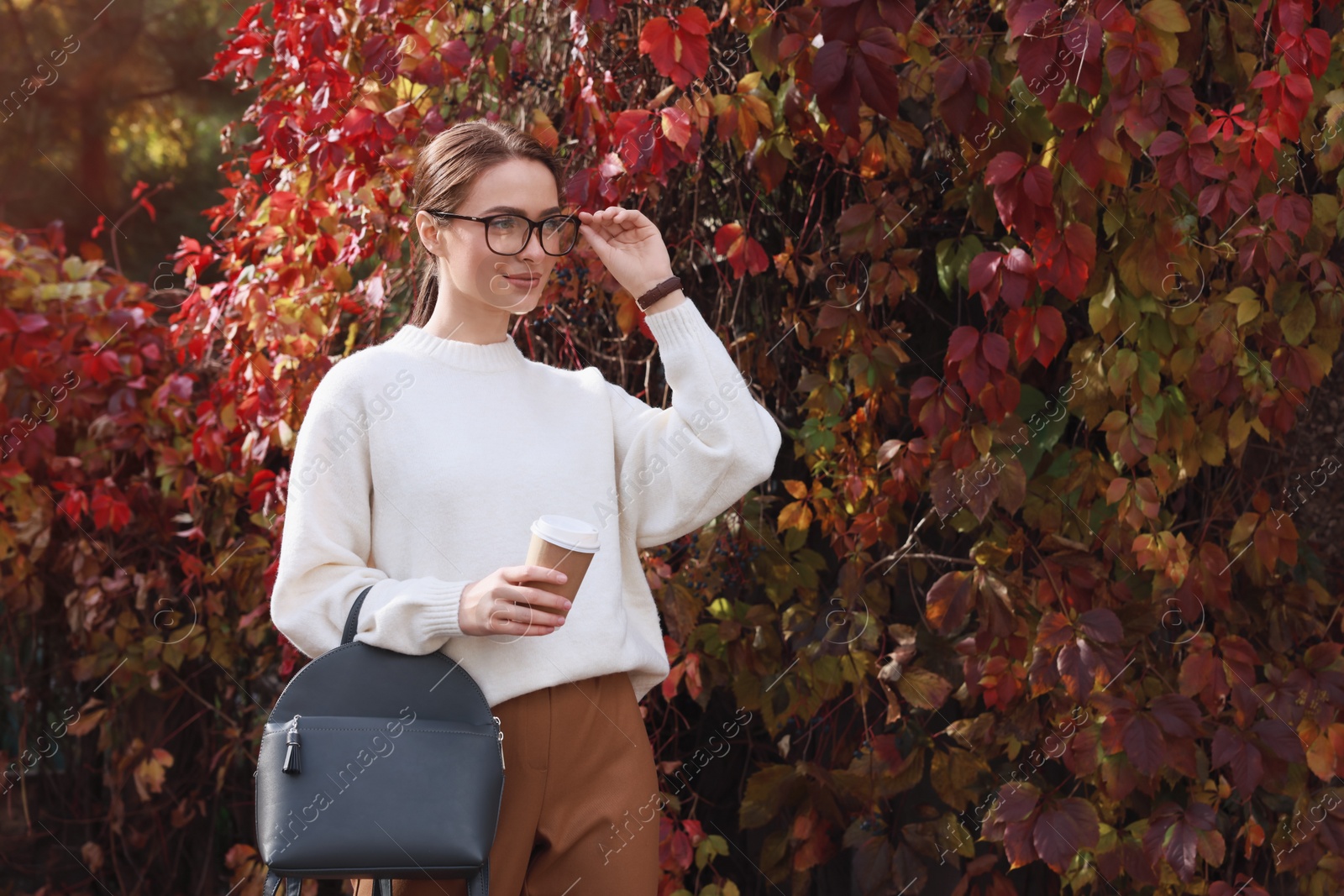 Photo of Beautiful young woman with stylish grey backpack and hot drink in autumn park