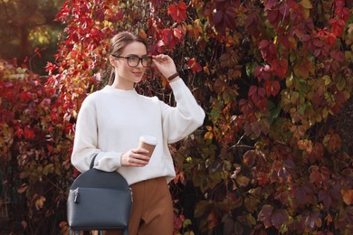 Photo of Beautiful young woman with stylish grey backpack and hot drink in autumn park