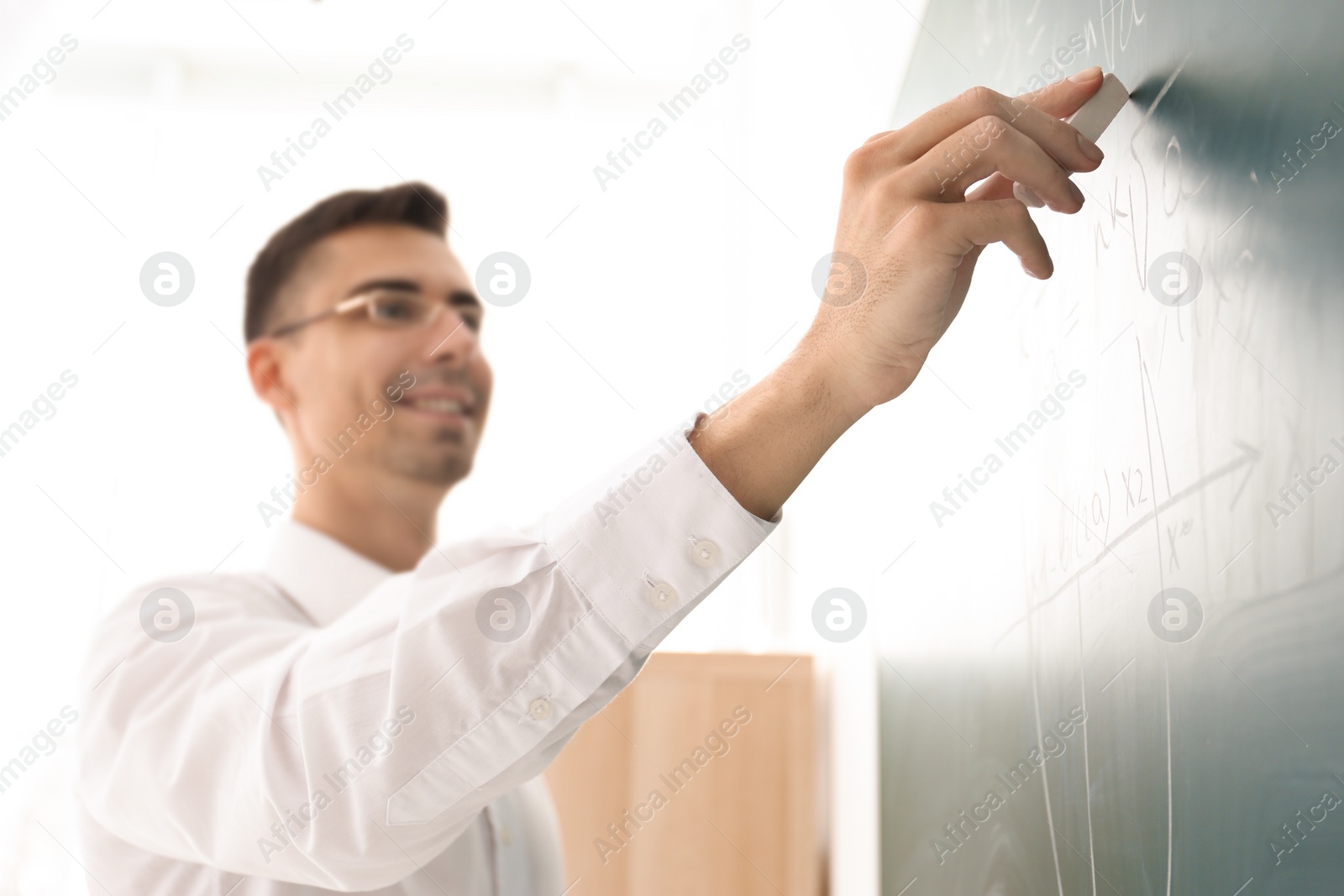 Photo of Young male teacher writing on blackboard in classroom