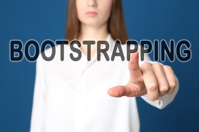 Image of Woman touching virtual screen with word BOOTSTRAPPING against blue background, focus on hand