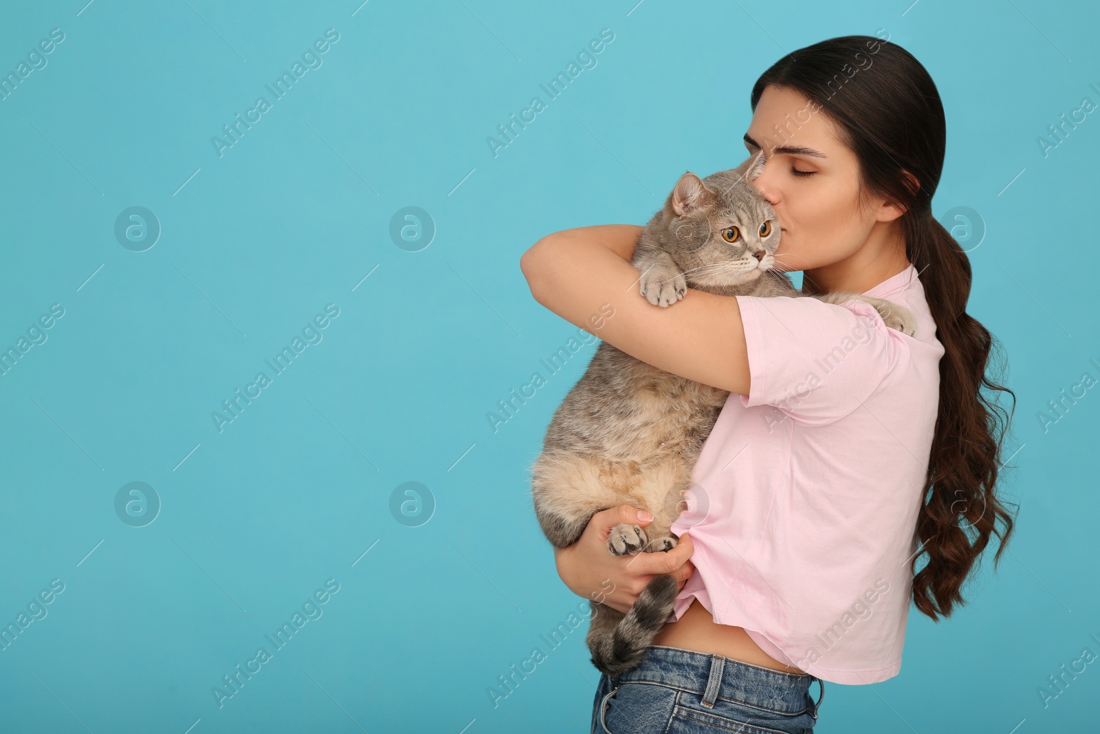 Photo of Young woman kissing her adorable cat on light blue background, space for text