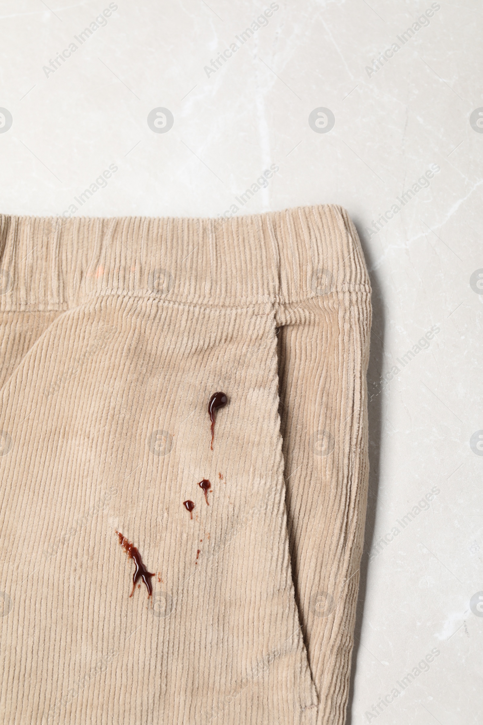 Photo of Dirty pants with stains of chocolate on light grey marble table, top view