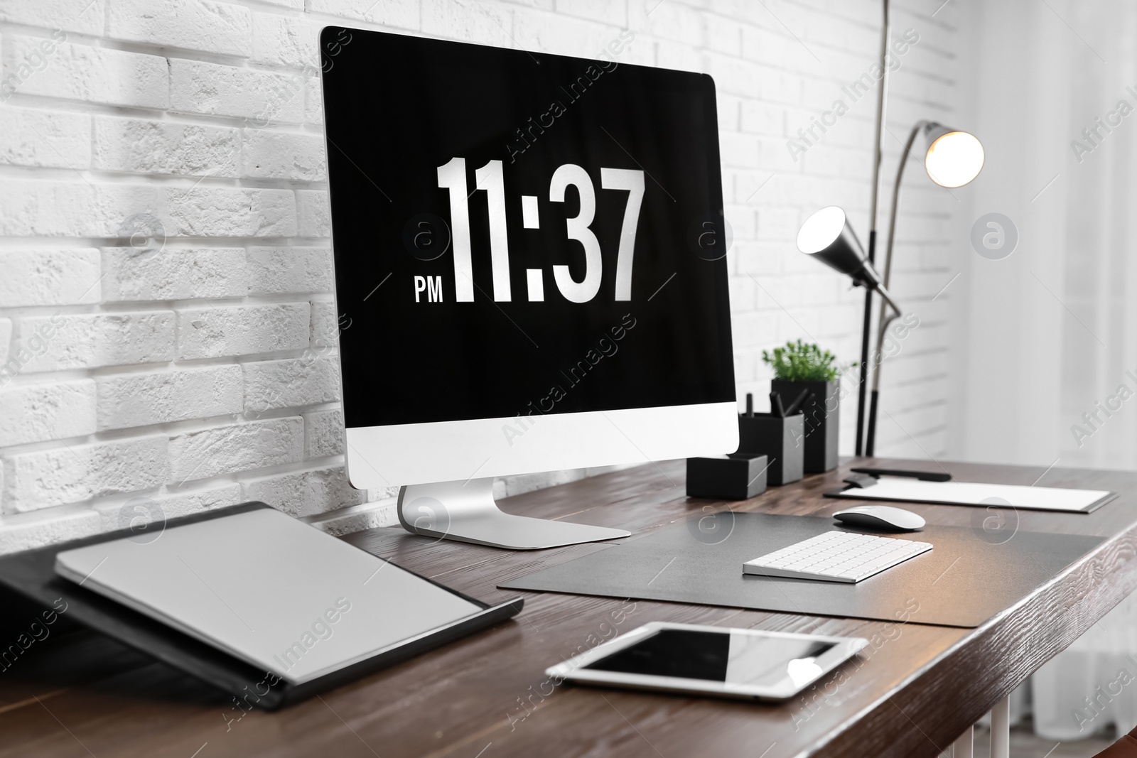 Photo of Modern workplace interior with computer and devices on table near brick wall