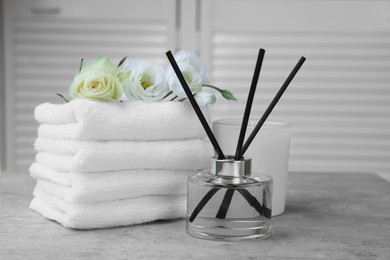 Towels, reed air freshener, scented candle and flowers on grey table indoors