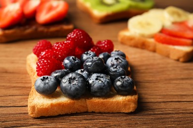 Tasty toast with berries on wooden table, closeup