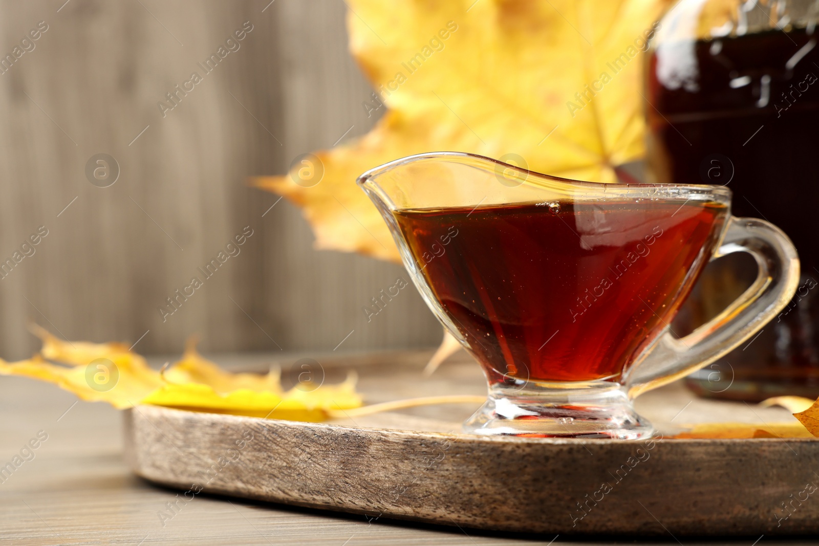 Photo of Gravy boat and bottle of tasty maple syrup on wooden table, closeup. Space for text