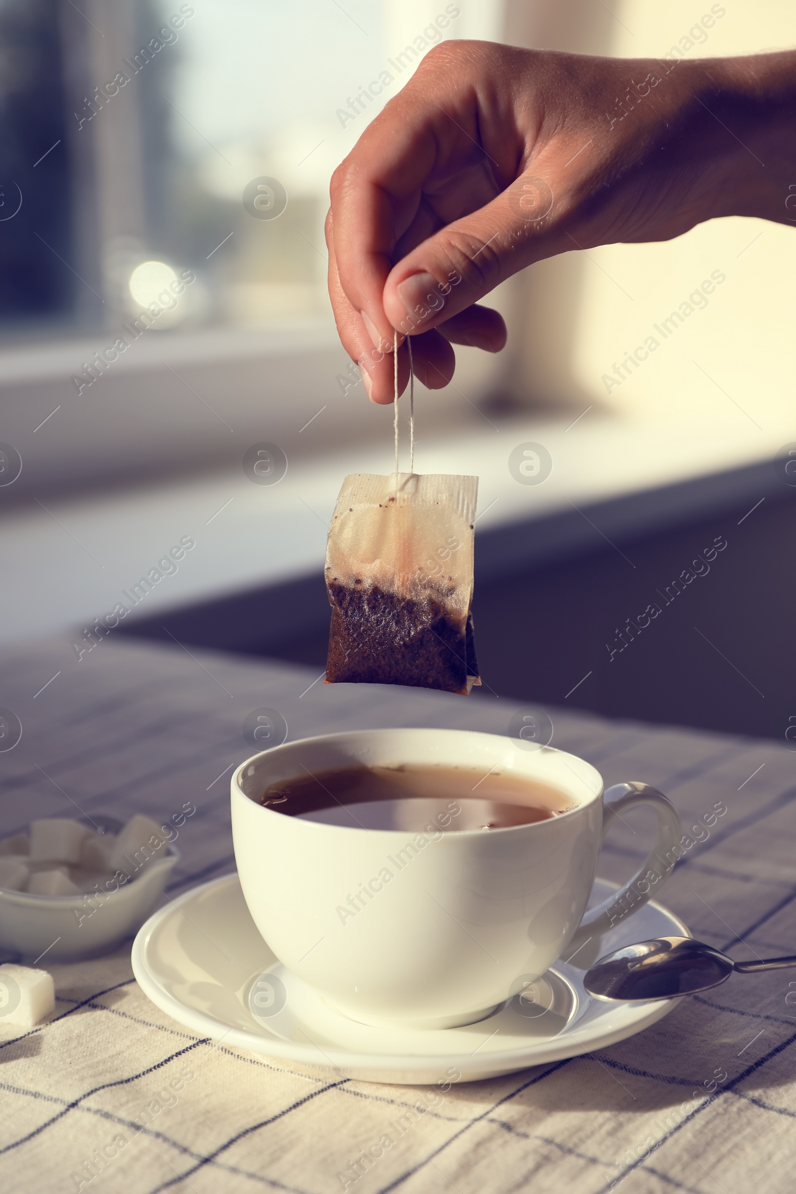 Photo of Woman taking tea bag out of cup at table indoors, closeup