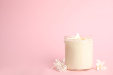 Photo of Beautiful candle with wooden wick and flowers on pink background, space for text