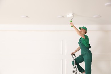 Photo of Worker painting ceiling with white dye indoors, space for text