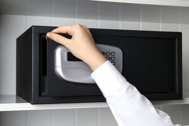 Photo of Woman opening black steel safe with electronic lock, closeup