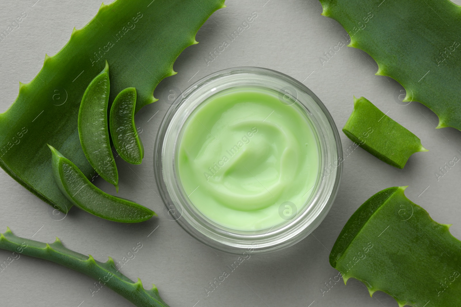 Photo of Jar with cream and cut aloe leaves on light grey background, flat lay