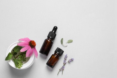 Bottles of essential oils, different herbs and flowers on white background, flat lay. Space for text