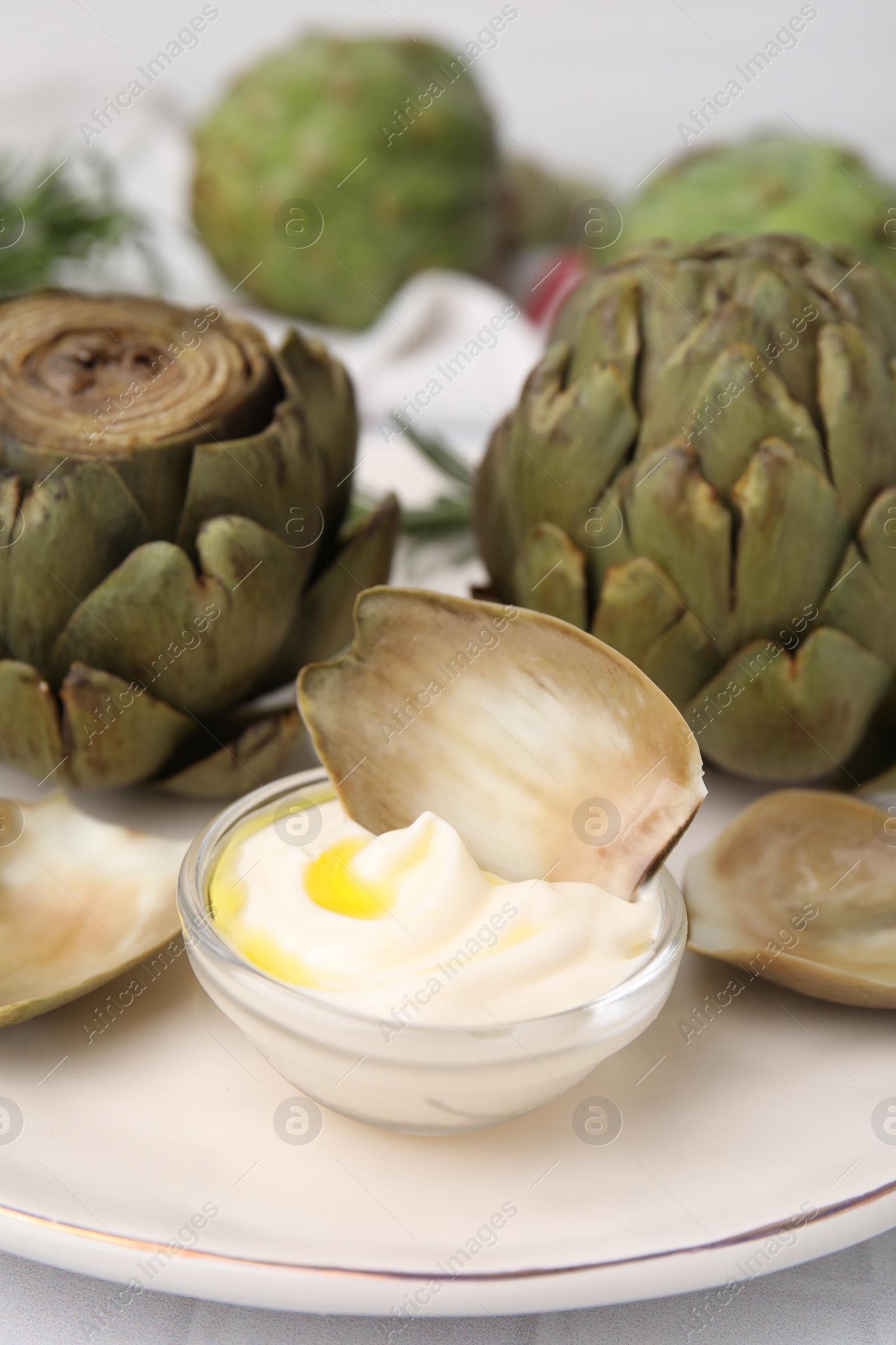 Photo of Delicious cooked artichokes with tasty sauce served on plate, closeup