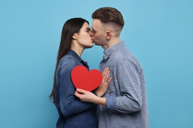 Photo of Lovely couple with decorative heart kissing on light blue background. Valentine's day celebration