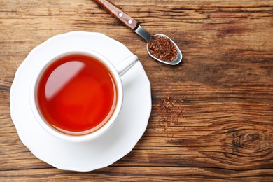 Freshly brewed rooibos tea, dry leaves and spoon on wooden table, flat lay. Space for text