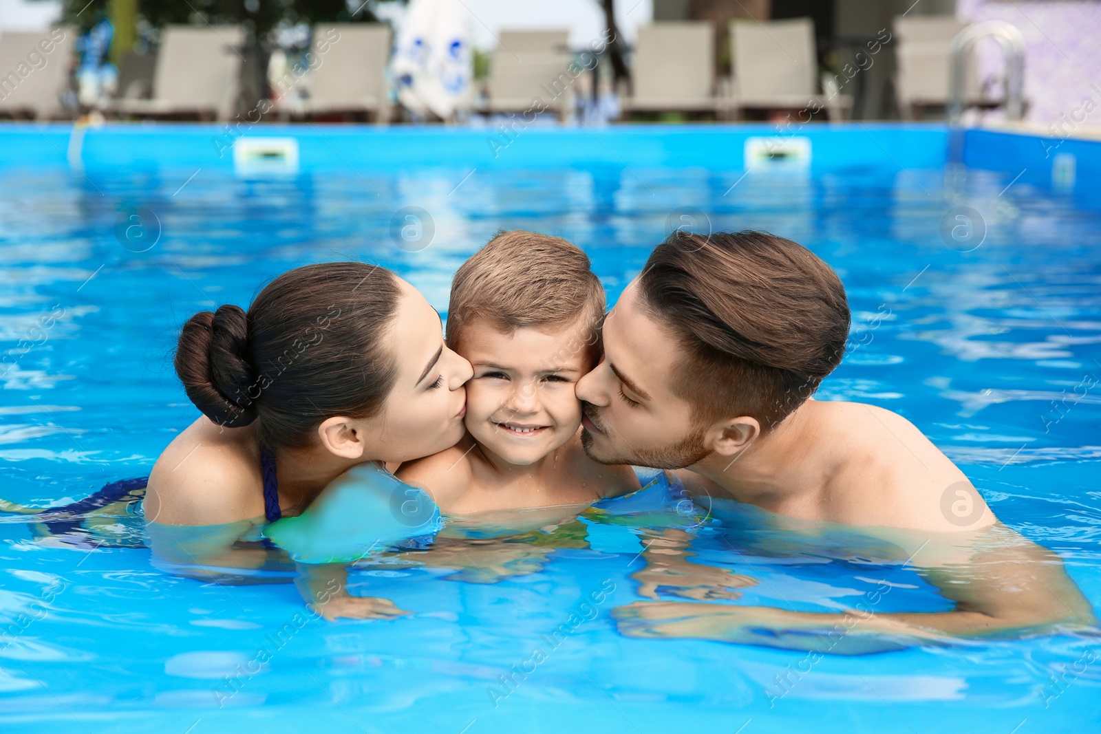 Photo of Young family with little son in swimming pool on sunny day