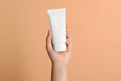 Photo of Woman holding tube of face cream on coral background, closeup