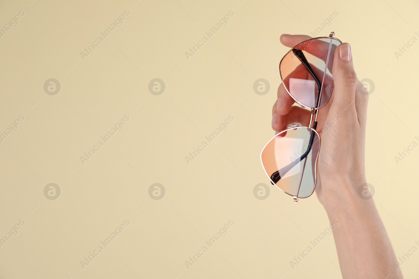 Photo of Woman holding stylish sunglasses on beige background, closeup. Space for text