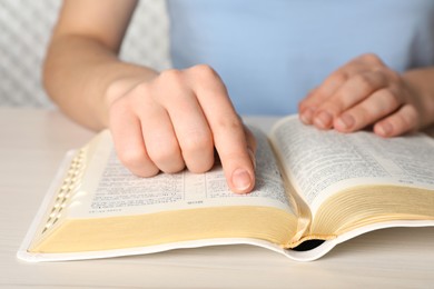 Photo of Woman reading Bible at white wooden table, closeup