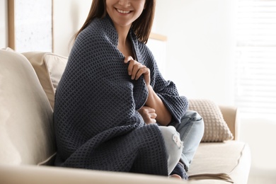 Photo of Woman covered with warm dark blue plaid sitting on sofa at home, closeup