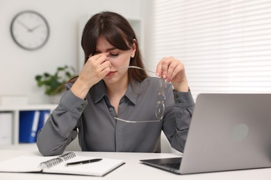 Overwhelmed woman sitting at table with laptop in office