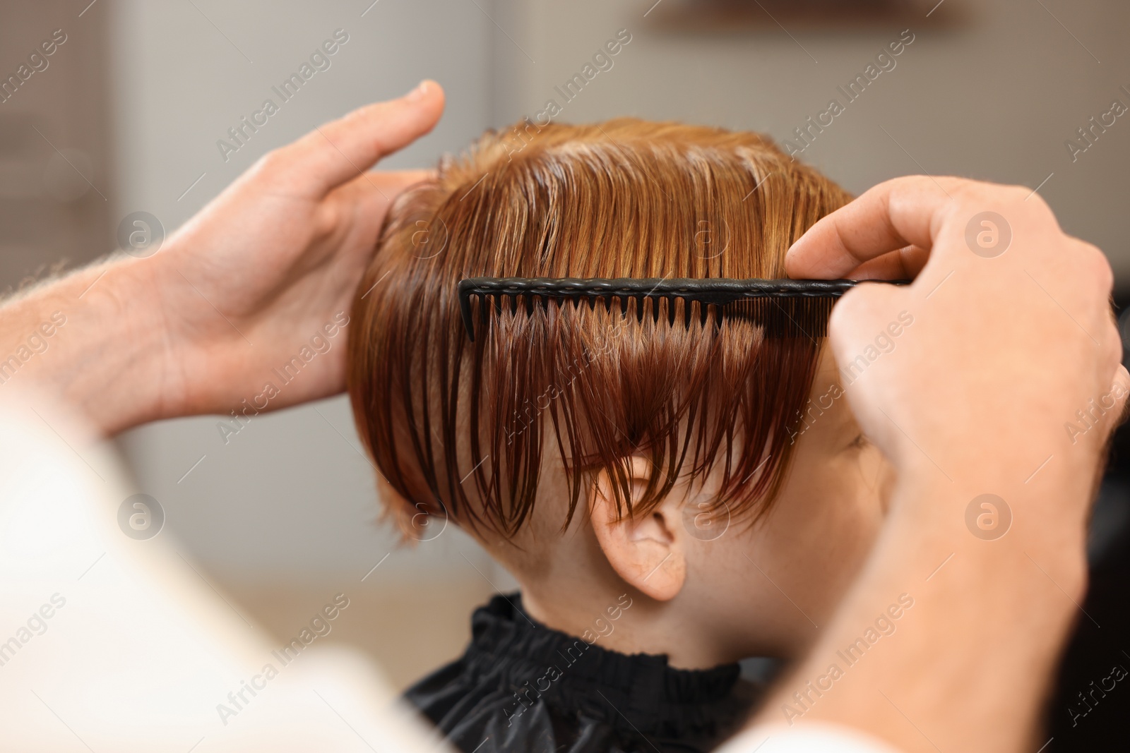 Photo of Professional hairdresser combing boy's hair in beauty salon, closeup