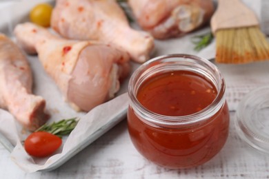 Photo of Marinade, basting brush and raw chicken drumsticks on white wooden table, closeup