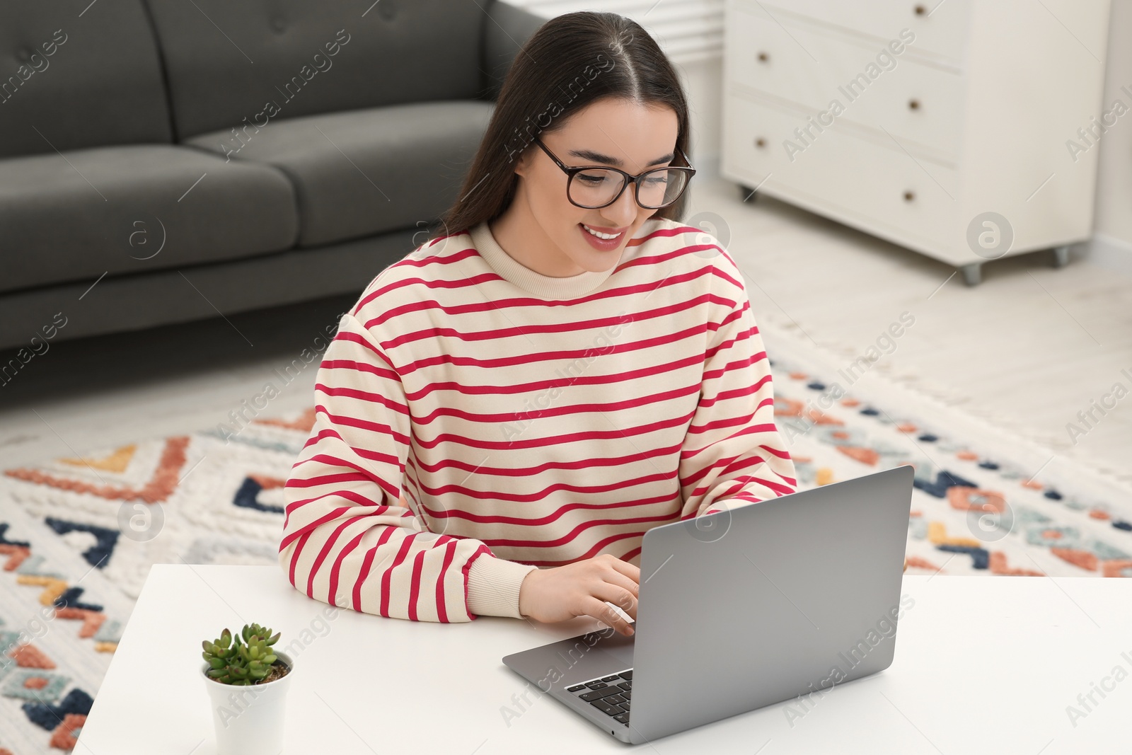 Photo of Woman using laptop at white table indoors