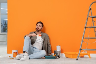 Photo of Designer sitting on floor near freshly painted orange wall indoors