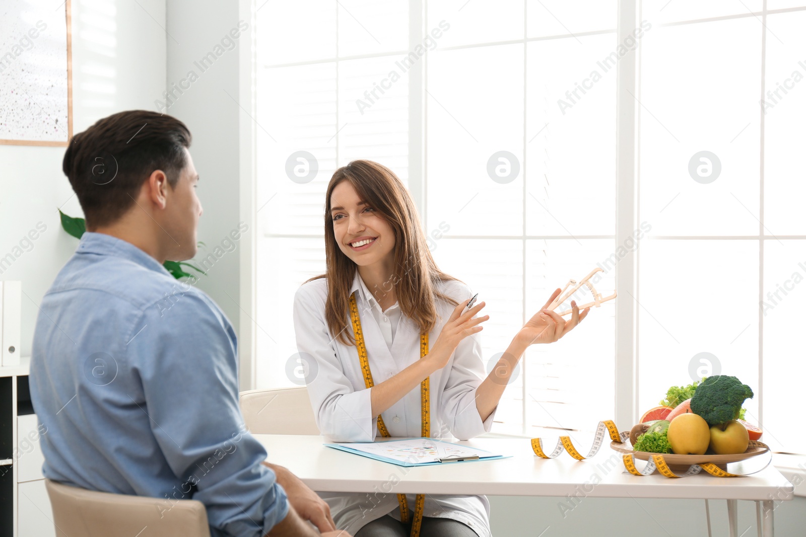 Photo of Young nutritionist consulting patient at table in clinic